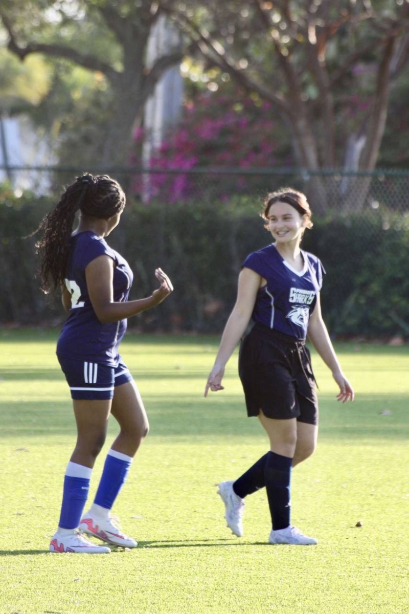 two students at PBMA smiling at each other dressed in soccer uniforms and walking on a soccer field