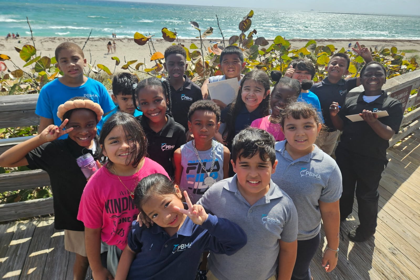 group of Palm Beach Maritime Academy charter school students smiling on a boardwalk next to the beach