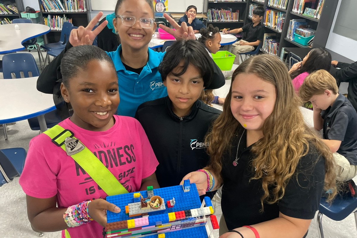 four students at PBMA charter school holding up a lego project and smiling in a classroom